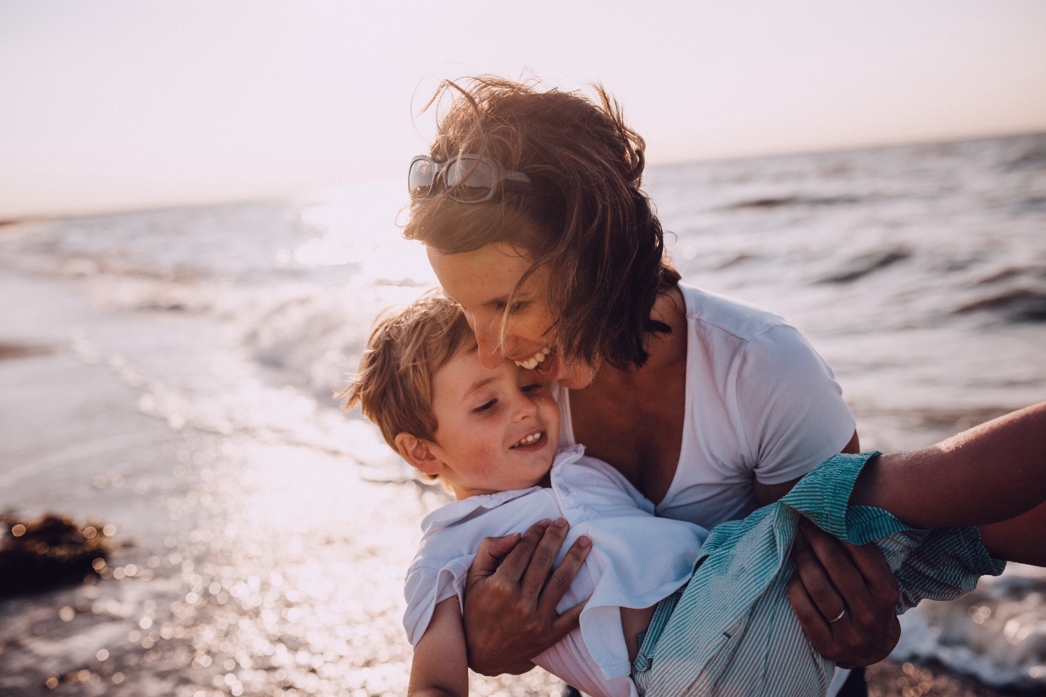 Woman holding young boy on a sunny beach next to the sea
