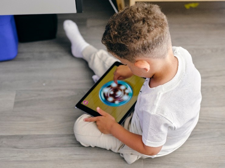 Boy sitting on floor holding and playing with tablet
