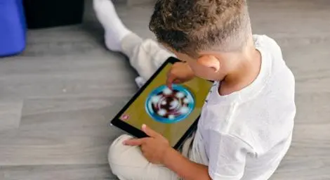 Boy sitting on floor holding and playing with tablet