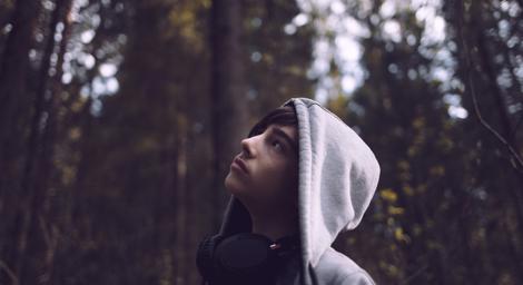 Teenage boy wearing a hoodie looking up into trees in a forest