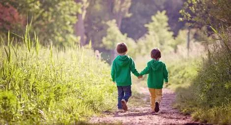 Two boys in green hoodies holding hands and walking down a forest path